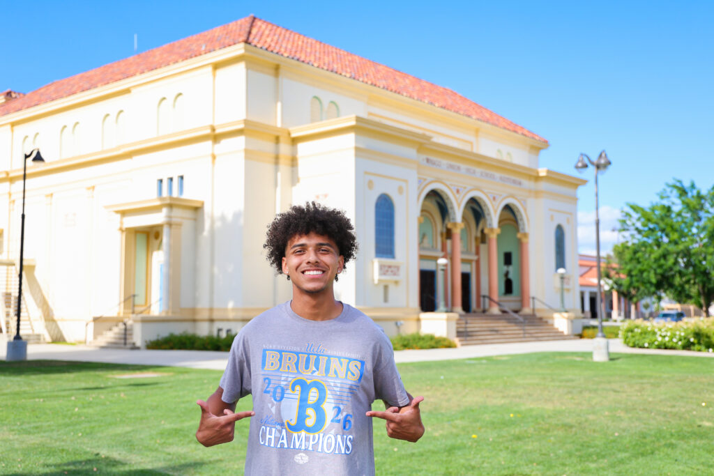 Braydon Ricks pointing to his UCLA shirt while standing outside Wasco High School. 