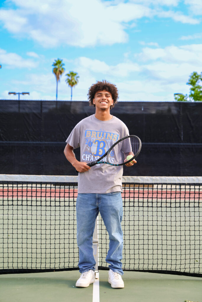 Braydon Ricks stands on the tennis court holding a tennis racket. 