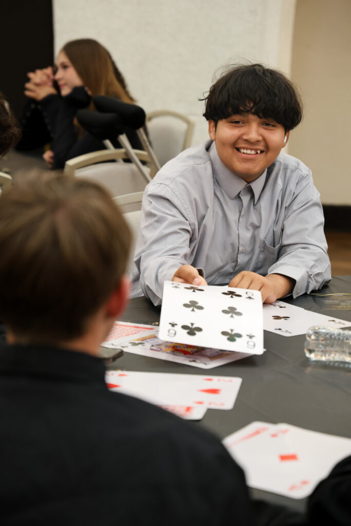 alt= "Student smiling while playing with oversized playing cards."
