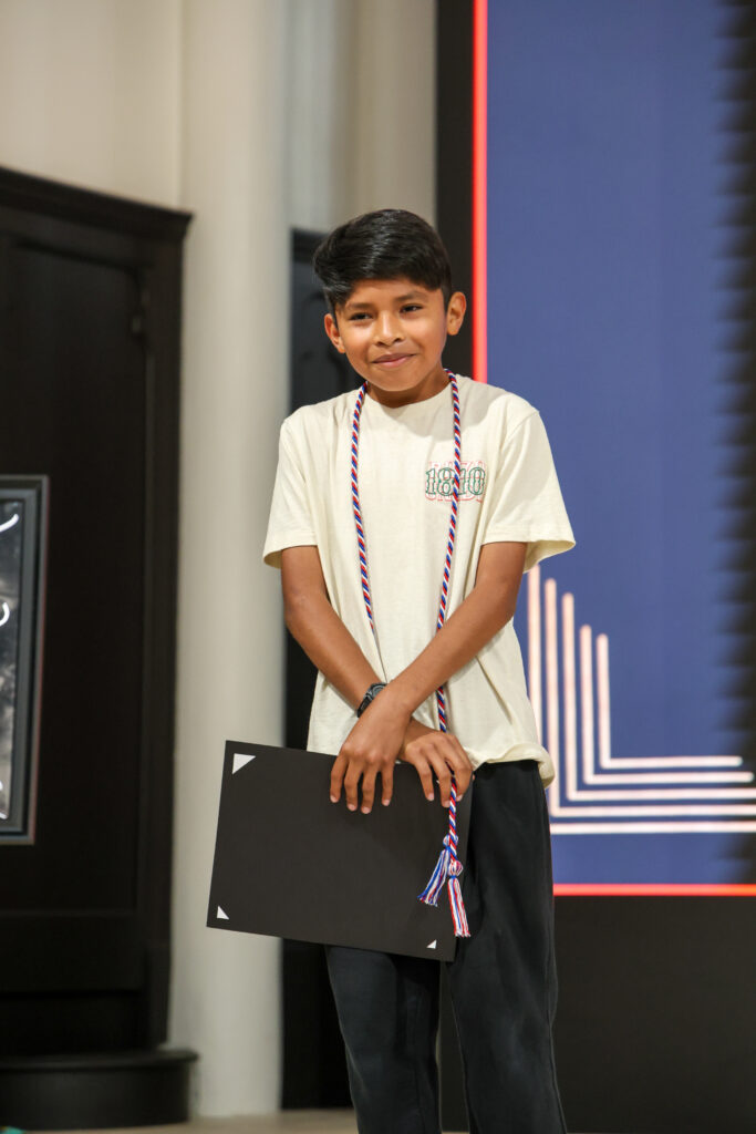 alt= "Middle school student smiling after receiving his cord and award certificate."