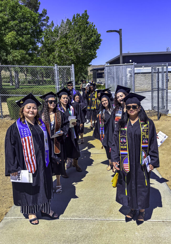 Photo of a group of graduates in their caps and gowns posing in a v formation ahead of their graduation ceremony.