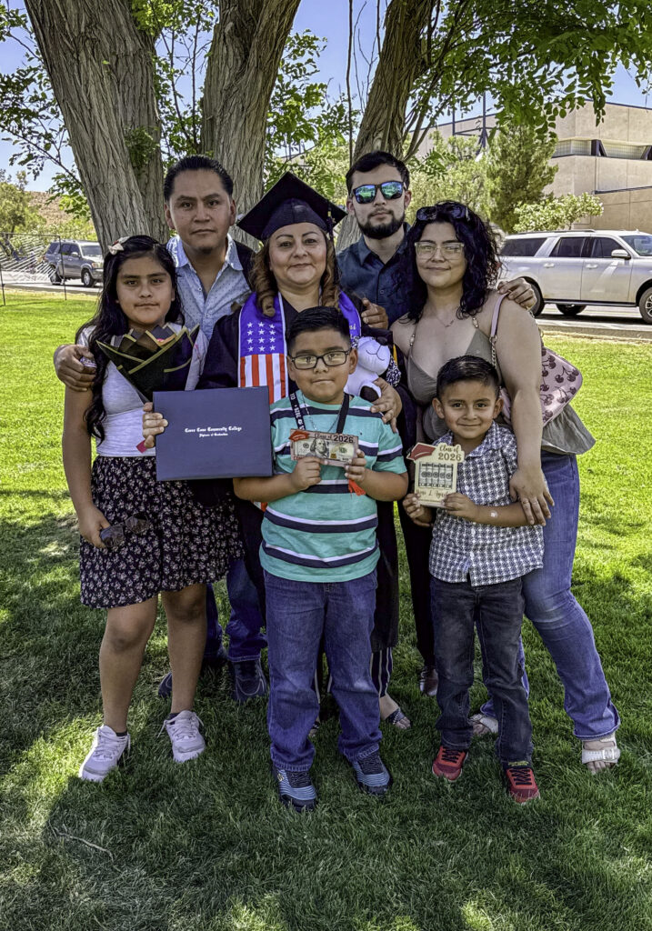 Photo of a graduate from the early child education cohort stands in her cap and gown with her certificate sounded by her family