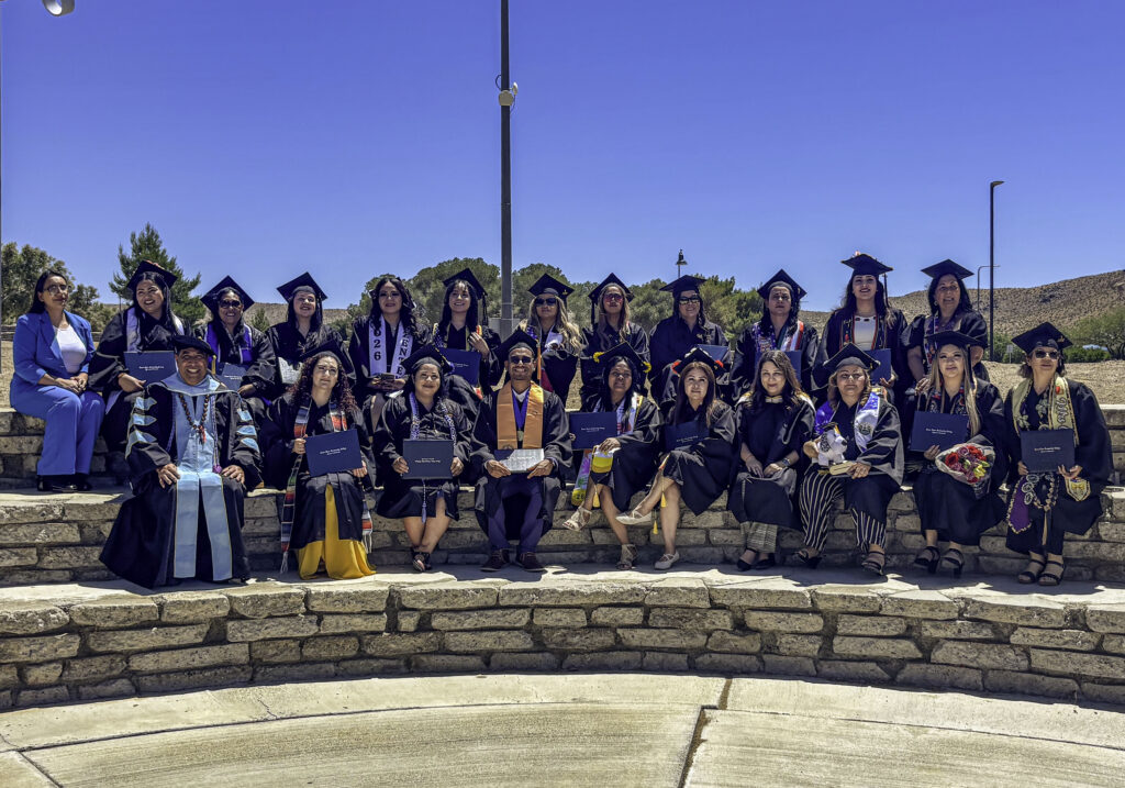 photo of 22 cohort graduates and their professors in their caps and gowns for the graduation ceremony sitting in two rows in an outside amphitheatre