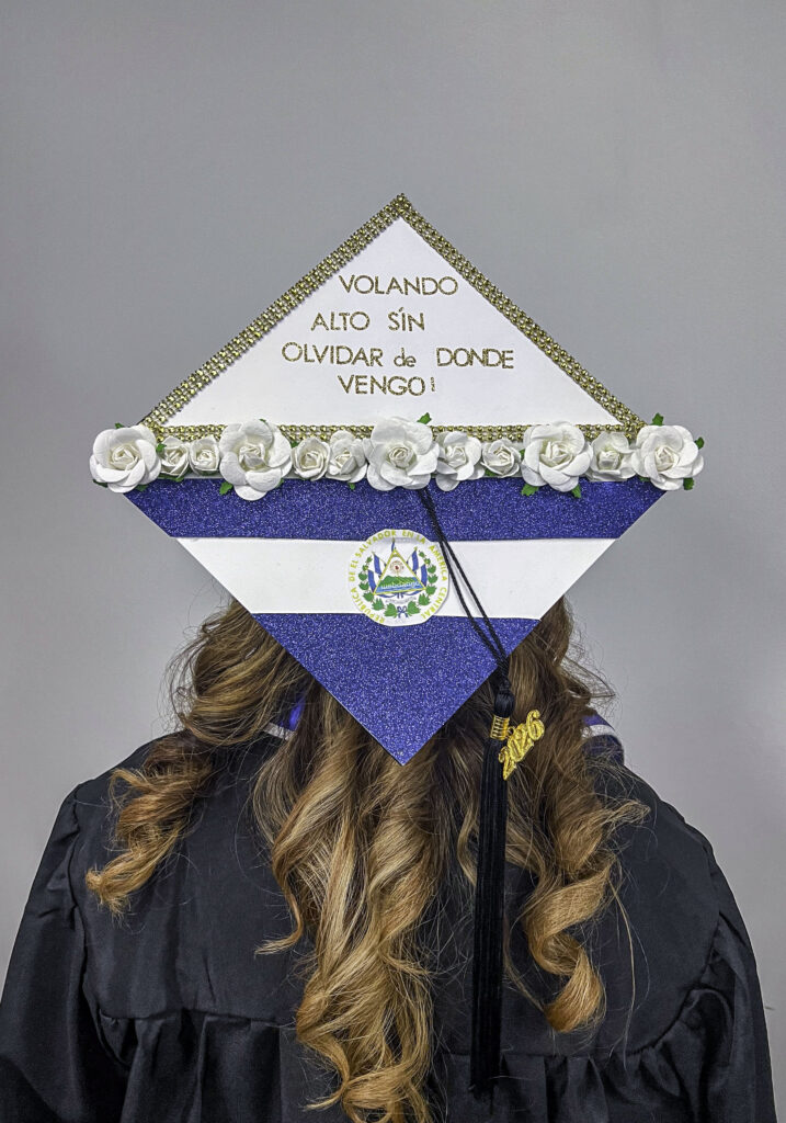 photo of a decorated graduation mortarboard with white flowers, the colored stripes of the El Salvador flag and the words "volando alto sin olvidar de donde vengo" which translates to "flying high without forgetting where I come from"