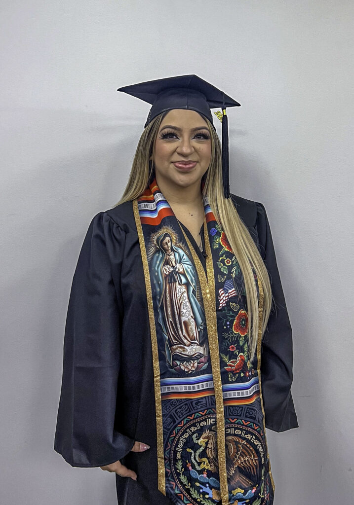 photo of a graduate posing in her cap and gown wearing a decorative sash.