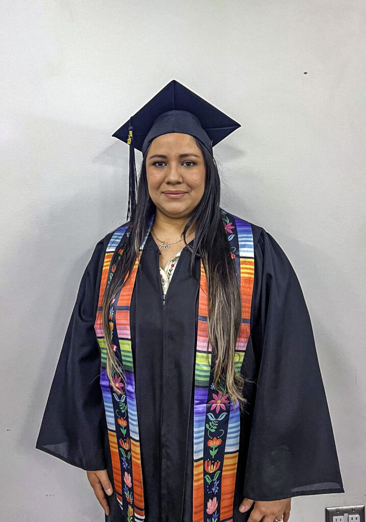 photo of a graduate posing in her cap and gown wearing a decorative sash.