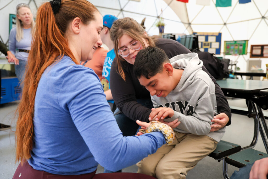 Naturalist holding a snake while a student pets it.