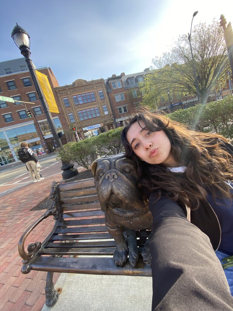 Photo of Acosta Vasquez siting next to a french bulldog statue of Yale's mascot.