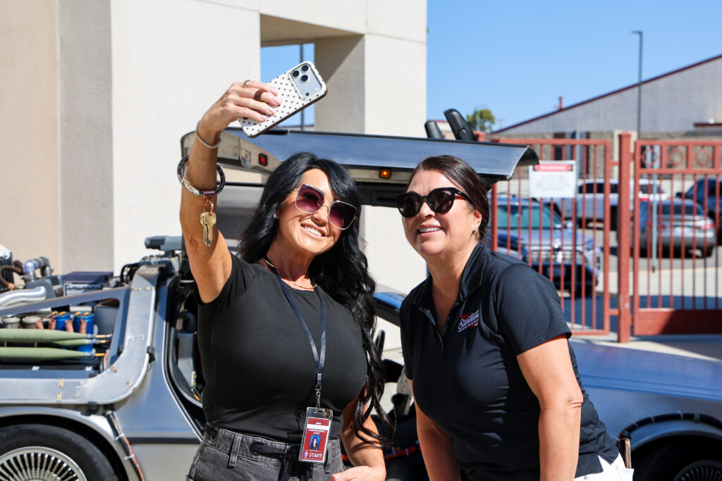 Two educators taking a selfie in front of DeLorean time machine inspired by the iconic Back to the Future films.