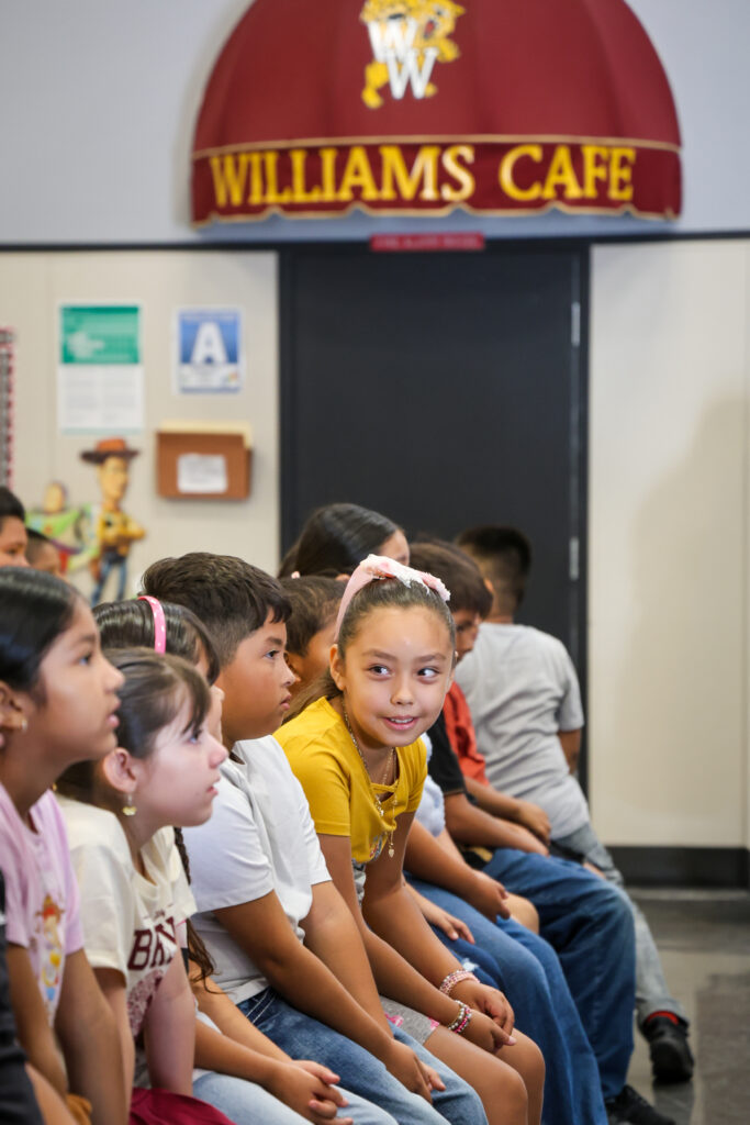 Students talking during the assembly in front of a Williams Cafe Sign.