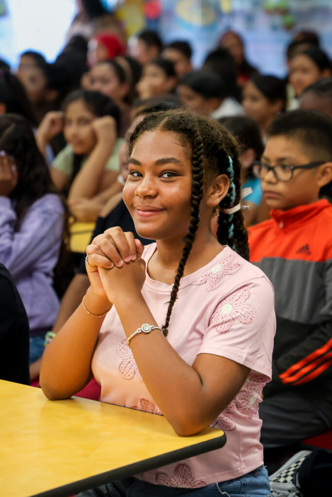 Female student smiling directly at the camera during the school assembly.