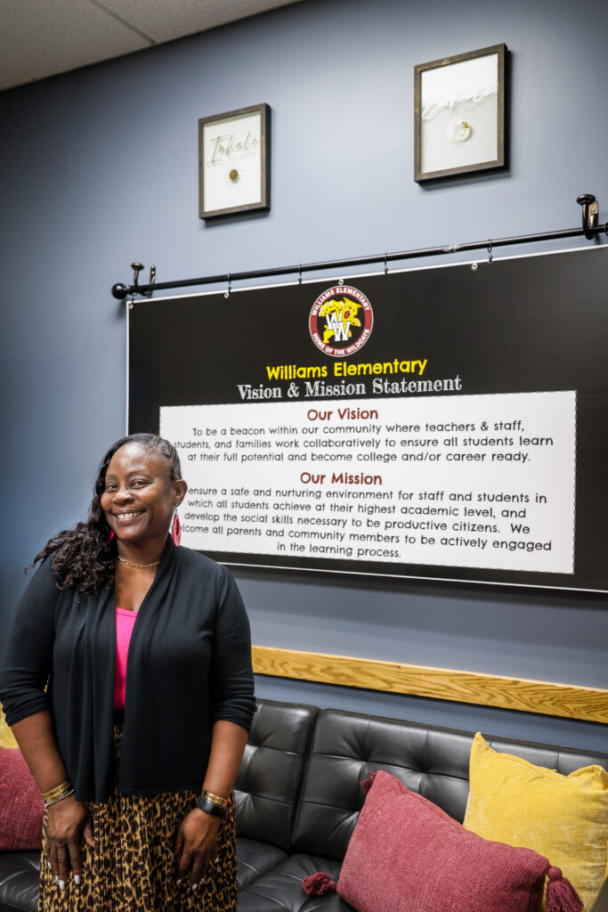 Principal Owens smiling in front of Williams Elementary mission and vision statement poster.