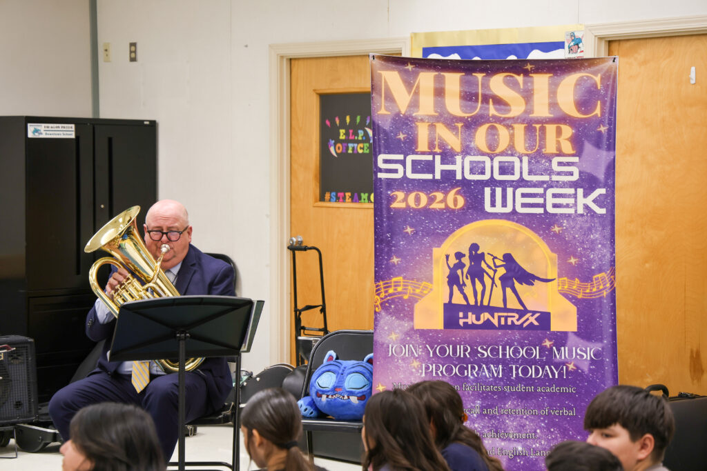 Michael Stone performing on the baritone next to a poster featuring the main characters from the movie K-Pop Demon Hunters.. 