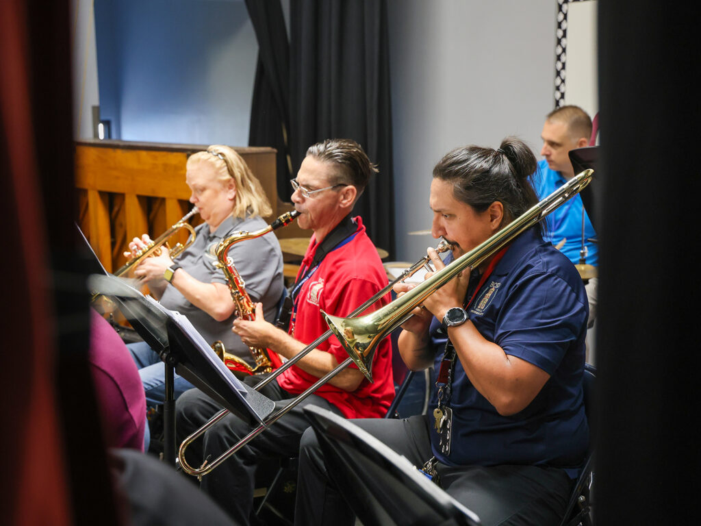 Three music teachers performing on the trombone, saxophone, and trumpet. All three teachers are wearing their school polo.